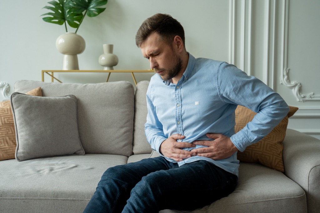 man-suffers-from-abdominal-pain-while-sitting-at-home-on-the-couch-picture-id1314592024